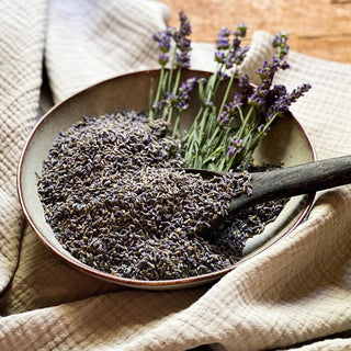 Dried lavender flowers fill a bowl that sits on a linen cloth. 