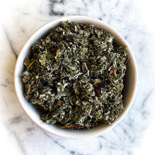 Dried red raspberry leaves in a white bowl on a white marble table.