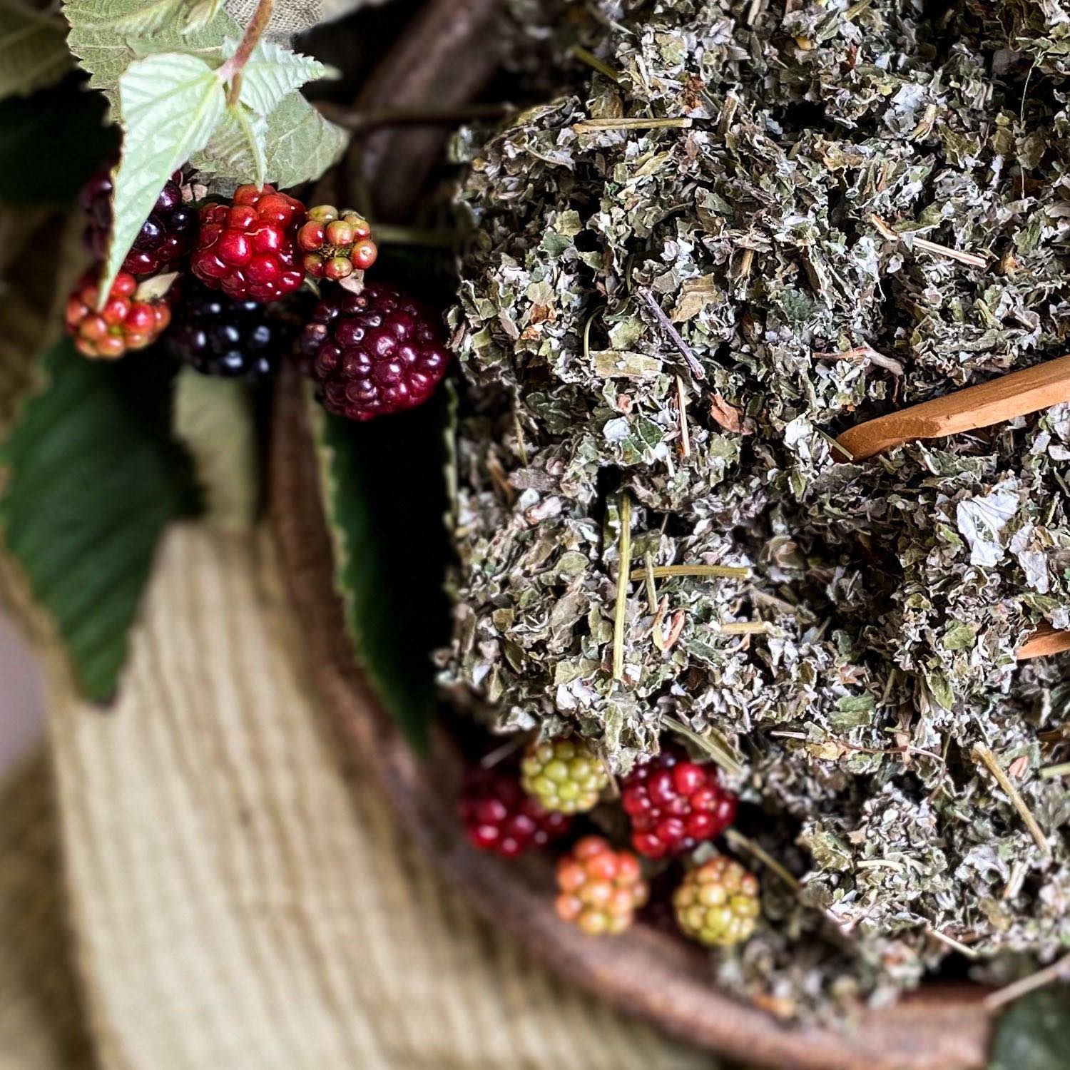 Dried red raspberry leaf in a wooden bowl surrounded by fresh berries.