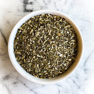 A white bowl filled with dried Yerba Mate tea sits on a white marble table.