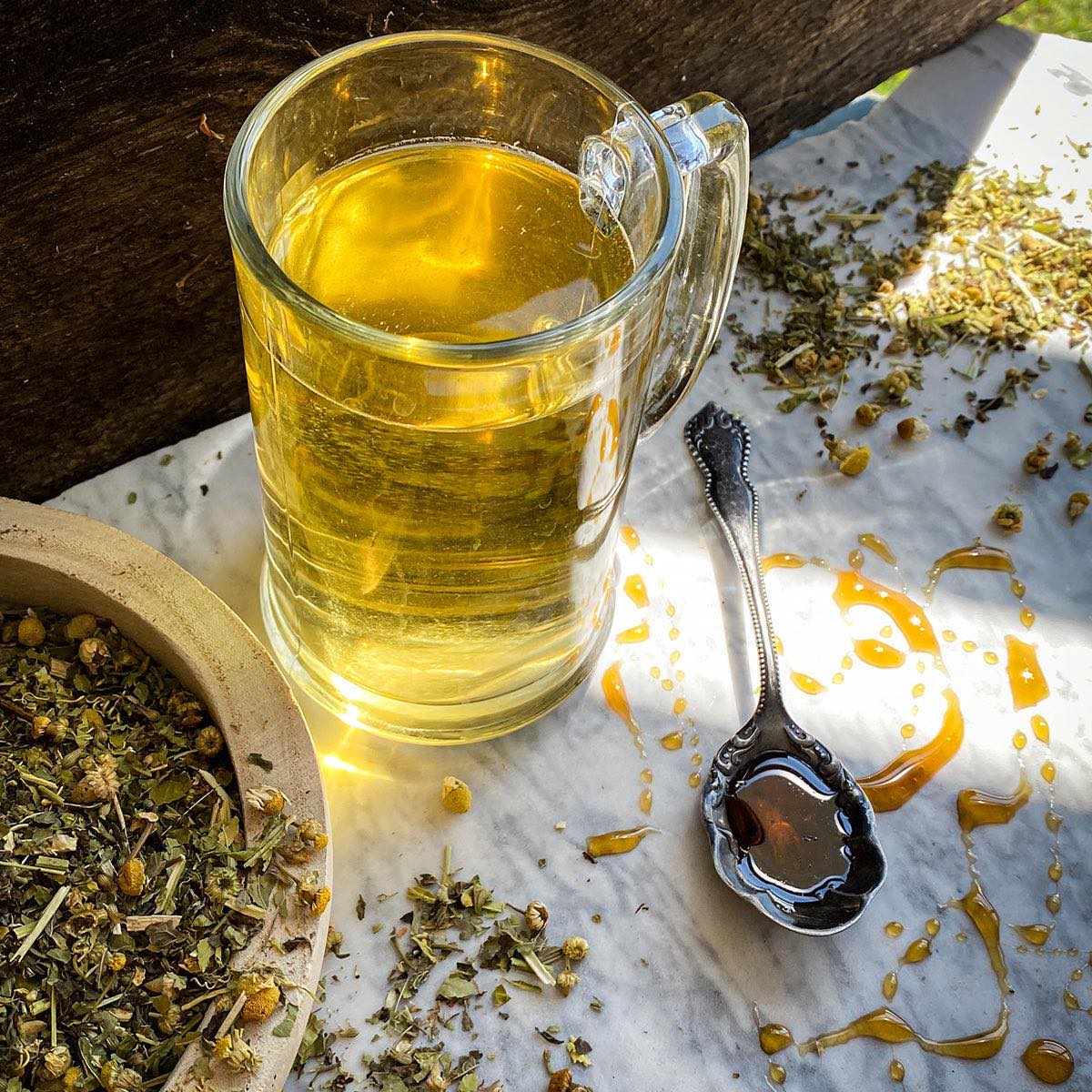 A brewed cup of Fast Asleep Tea rests on a marble surface with dried tea scattered about and a honey spoon.