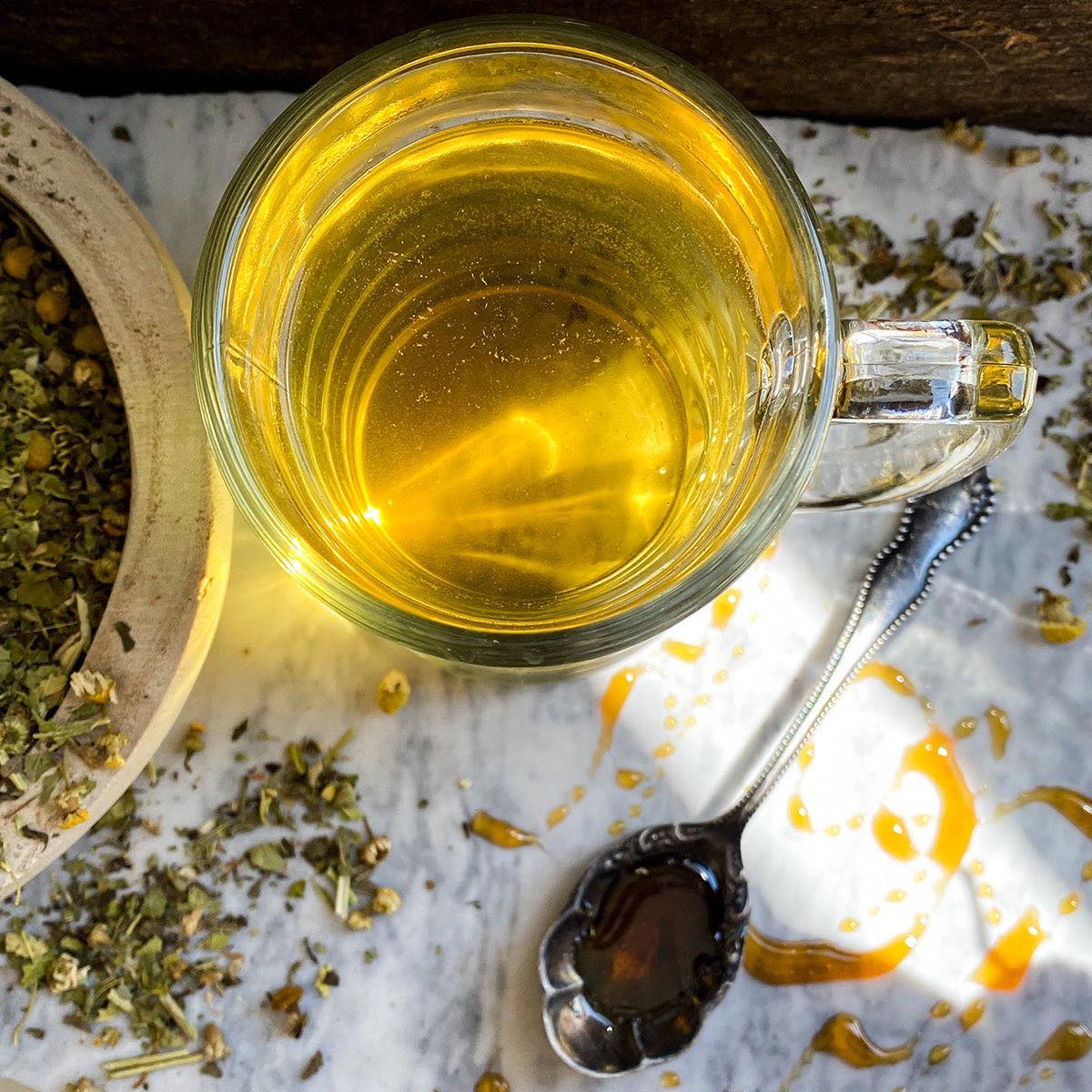 An overhead shot of the mug of brewed Fast Asleep Tea with dried herbs and a honey spoon.