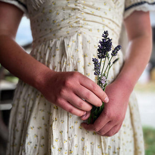 A girl holds a small bouquet of lavender flowers against her cream floral dress