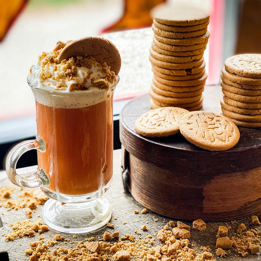 Brewed Gingersnap Tea in a glass mug with a whipped cream top and cookie crumble. A stack of cookies sit to the right of the brewed tea.