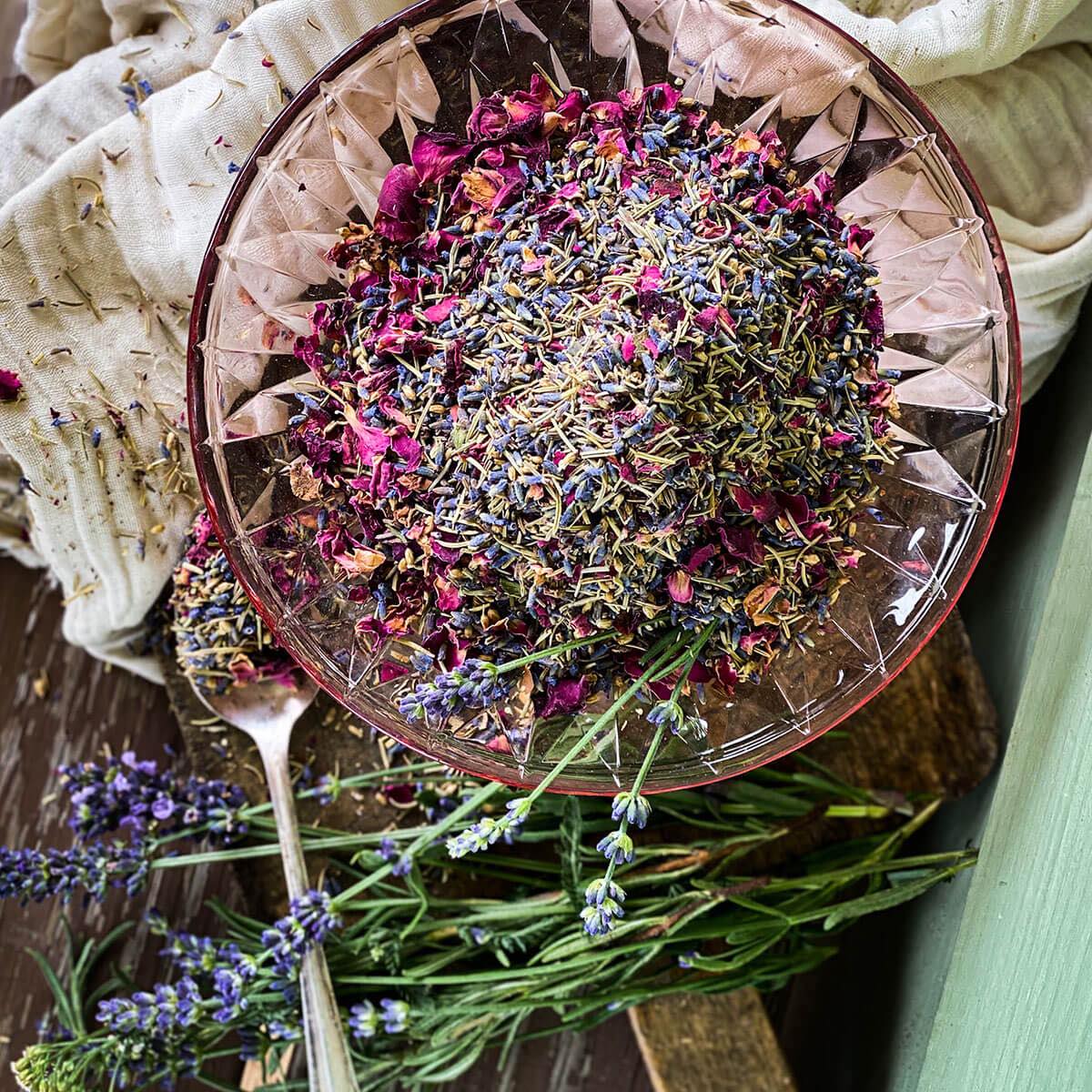 Herbal bath mix in a pink crystal bowl with fresh lavender and white cheesecloth in the background