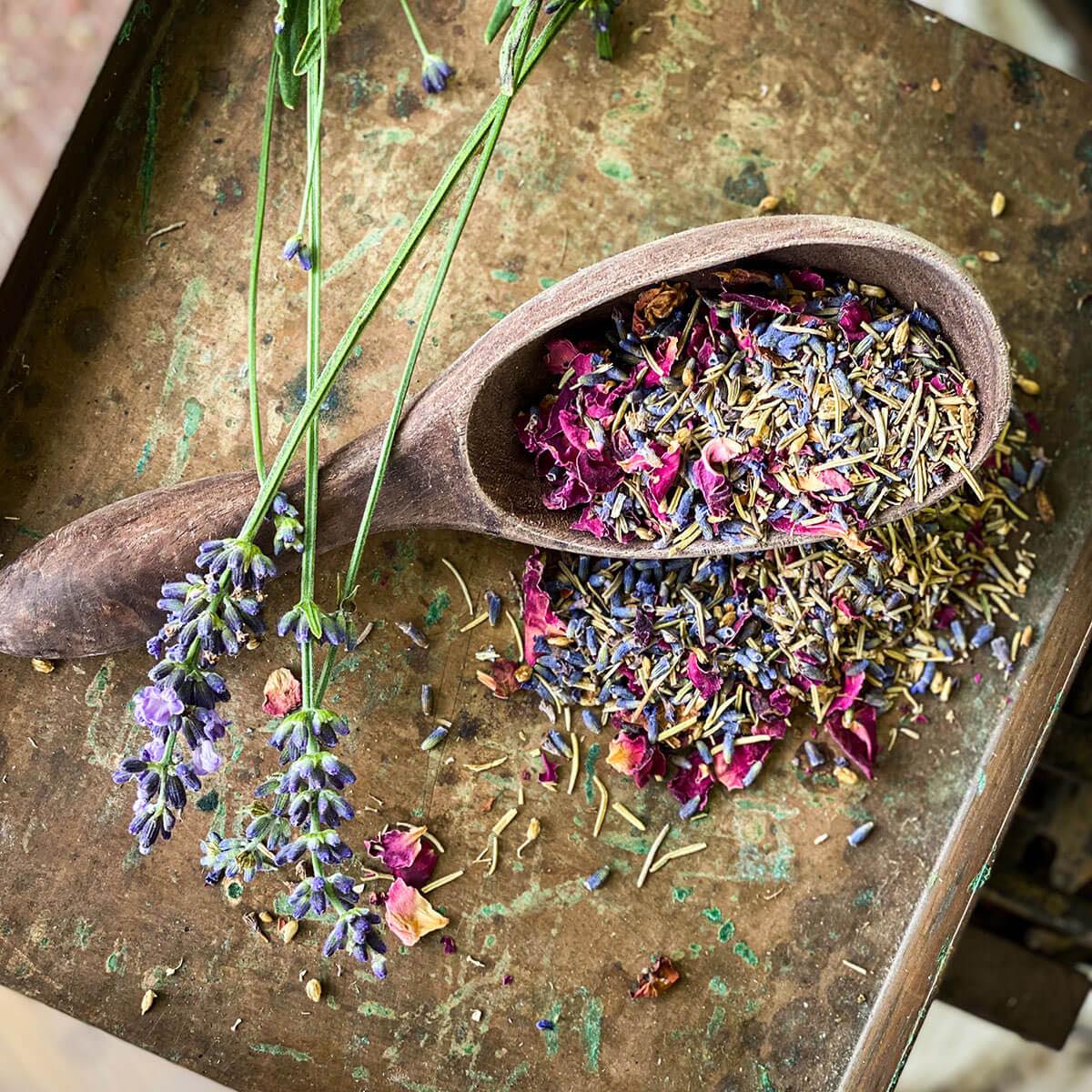 Herbal bath mix spills from a wooden spoon on a metal background with fresh lavender