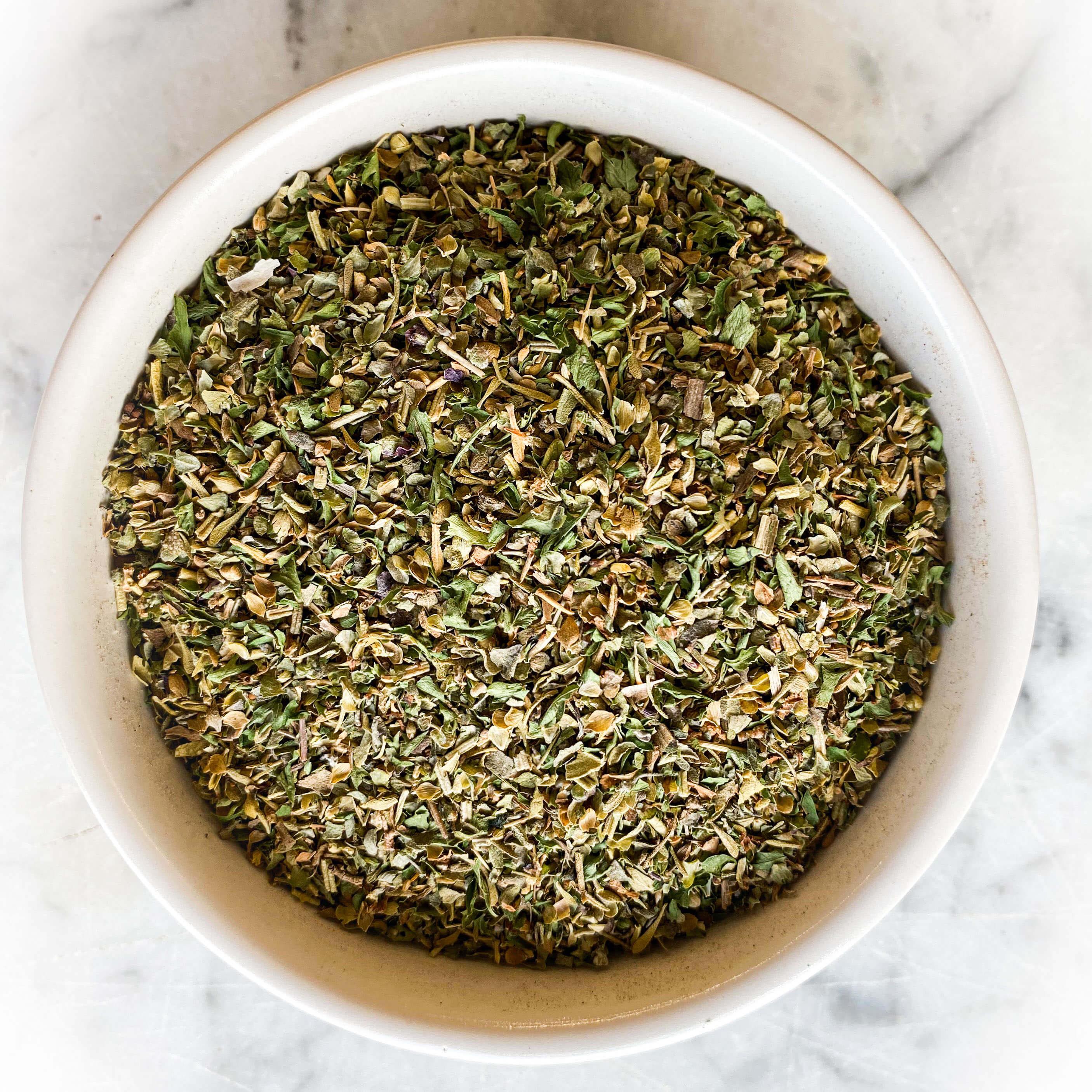 Italian Seasoning in a white bowl on a white marble background