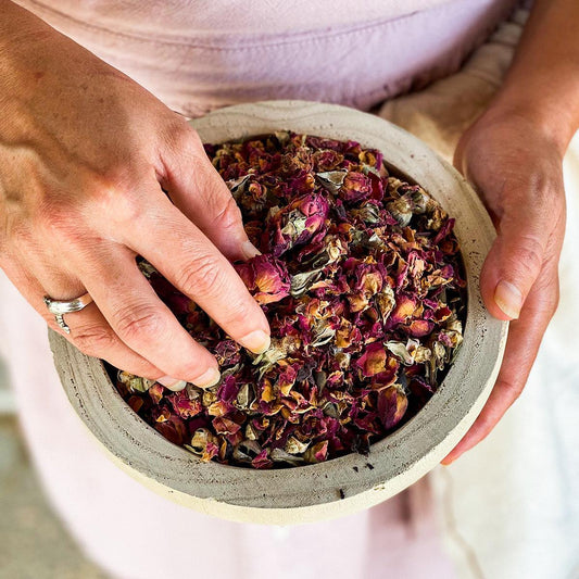 Red rose buds and petals in a wooden bowl held by a woman.