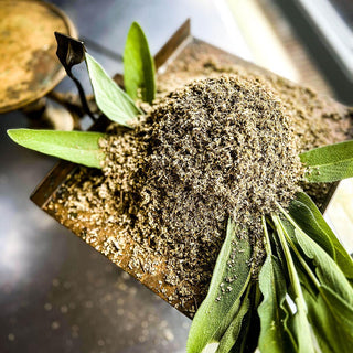 Dried and cut sage leaves sit atop an arranged display of fresh sage leaves on an antique scale.