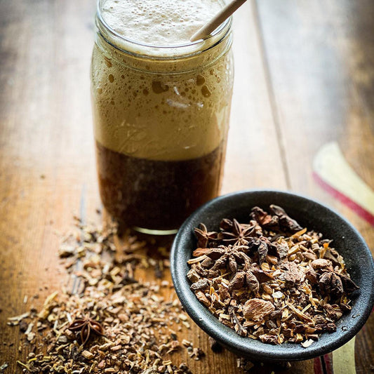 A bowl of dry sarsaparilla mix is in the foreground with a mason jar of the finished drink the background.