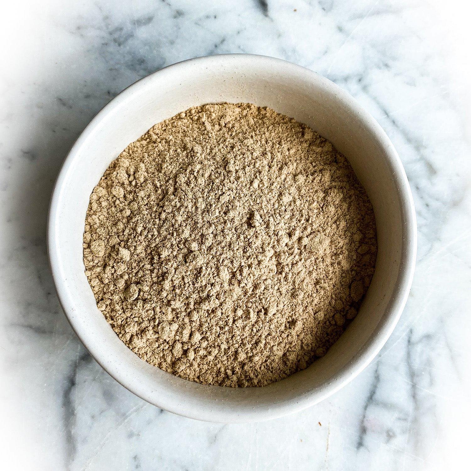 Dried slippery elm bark powder in a white bowl on a white marble background