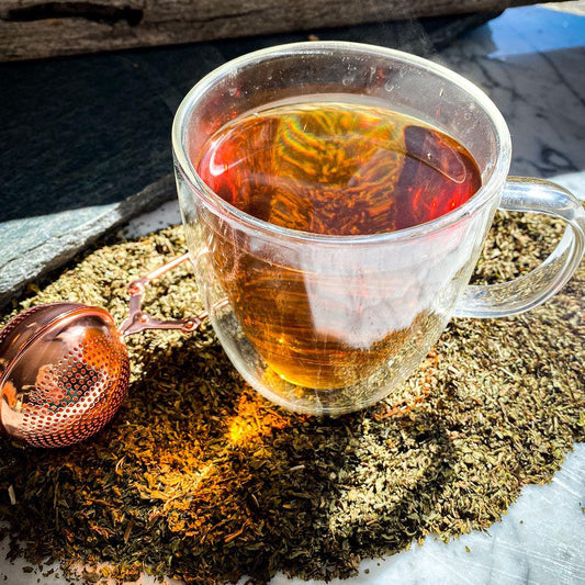 Spearmint leaf tea brewed in a glass mug with the dried leaves surrounding the mug.