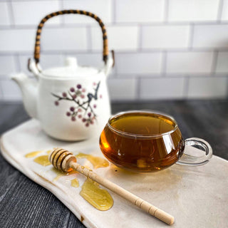Spearmint tea in a clear glass mug with a honey wand and white tea pot in the background.