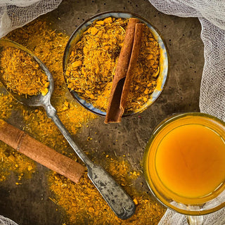 A bowl filled with dried tea and a cinnamon stick and a brewed cup of Turmeric Lemongrass Tea rets on a wood surface.