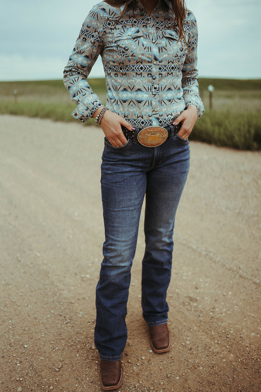 Woman standing on dirt road modeling the Womens Ultimate Riding Jean by Wrangler.  The style is Willow.