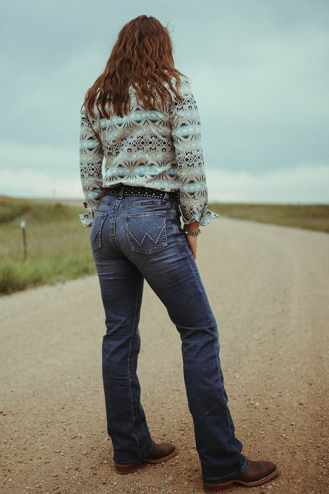 Women standing on dirt road modeling the Women's Ultimate Riding Jean by Wrangler.  2 back pockets.