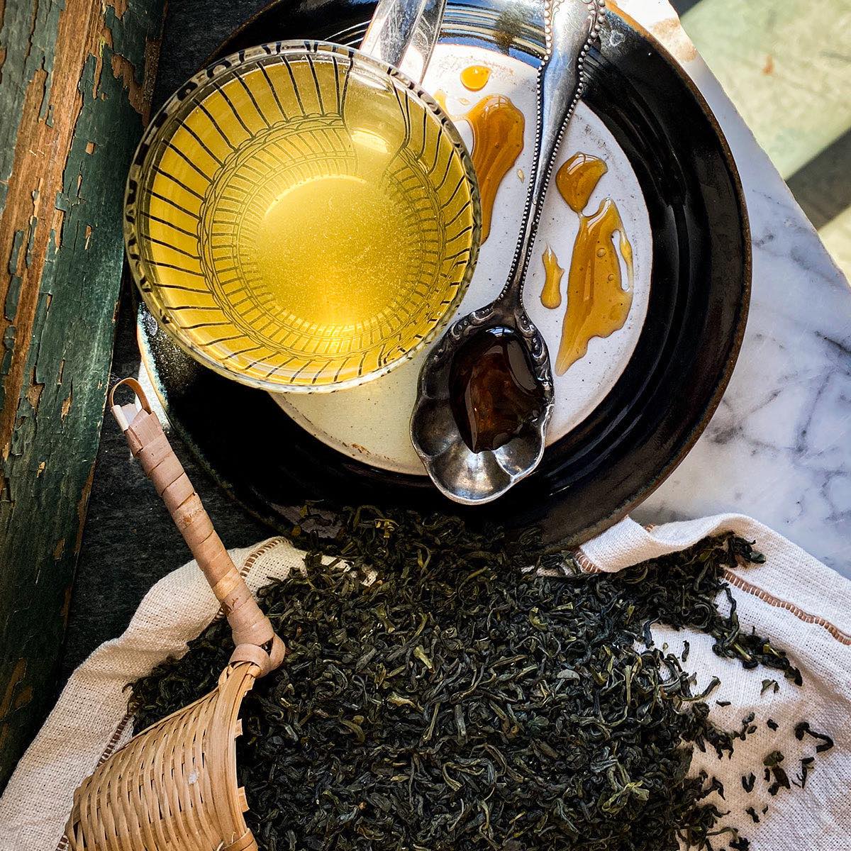 An overhead look of a brewed mug of Yun Wu Cloud Mist Tea with a tea strainer spilling the dried tea on the counter.