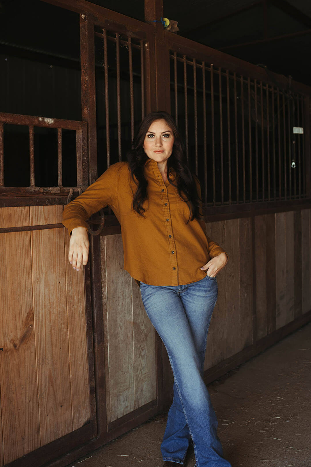 Woman standing in barn modeling the boyfriend flannel shirt in gold color.  The shirt is button up with collar.  