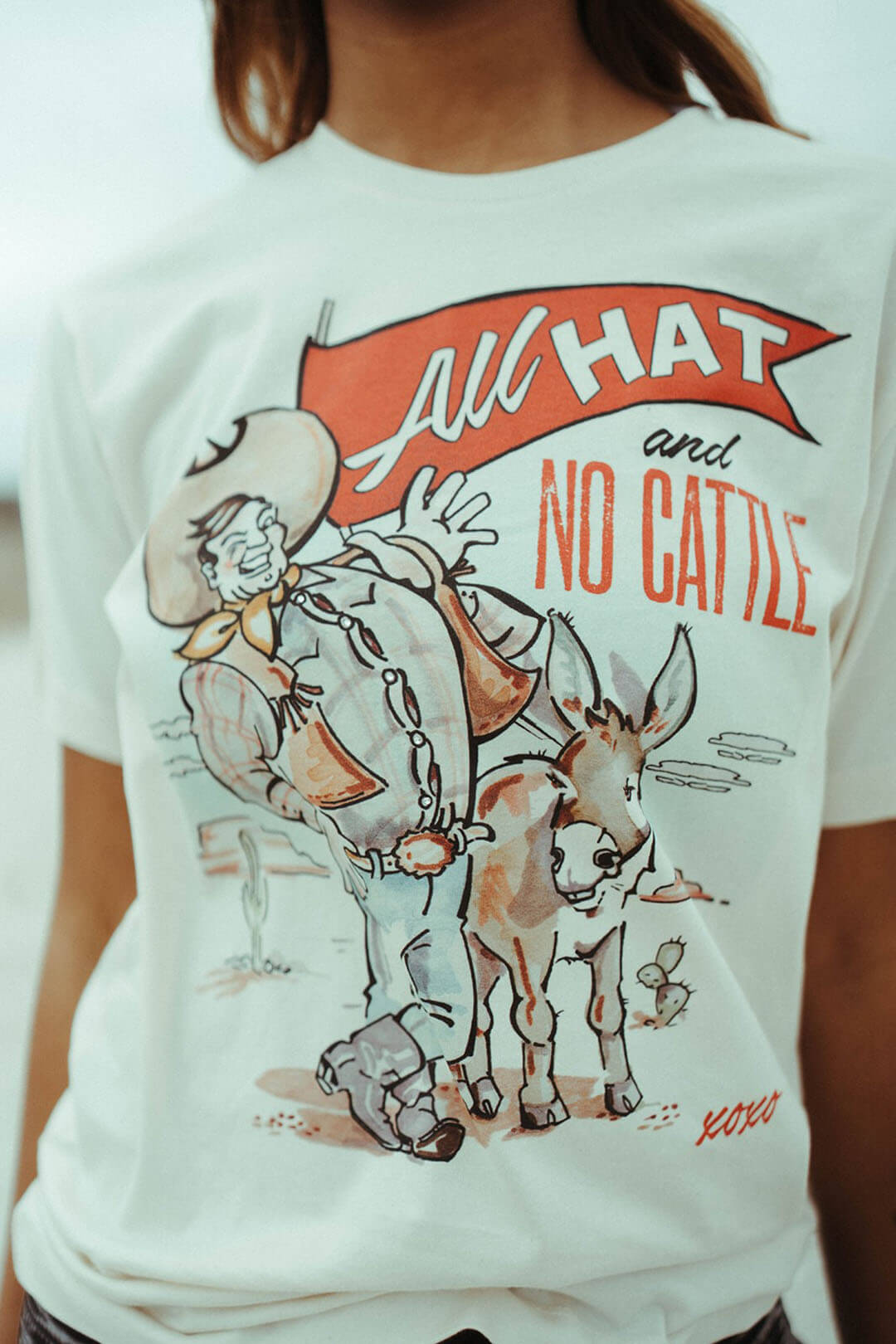 Close up picture of the XOXO art & company "All Hat and No Cattle" graphic tee shirt.  Made  and designed in Texas.   No shirt is the same. 