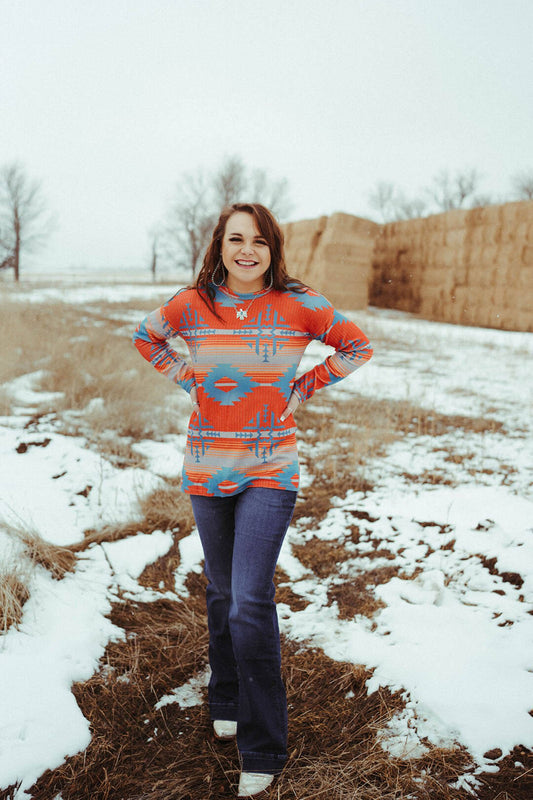Woman standing in snowy field next to hay bales.  She is wearing the Santa Fe Aztec Top.  