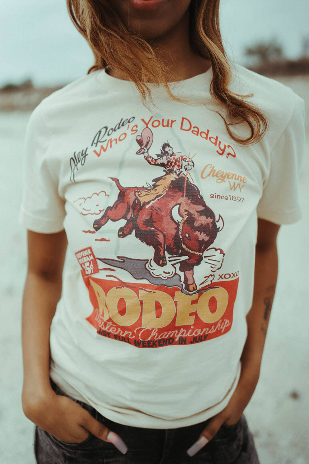Close up image of the Cheyenne Souenir Rodeo graphic tee from XOXO art & company.  The shirt says"Hey Rodeo, Whos Your Daddy?