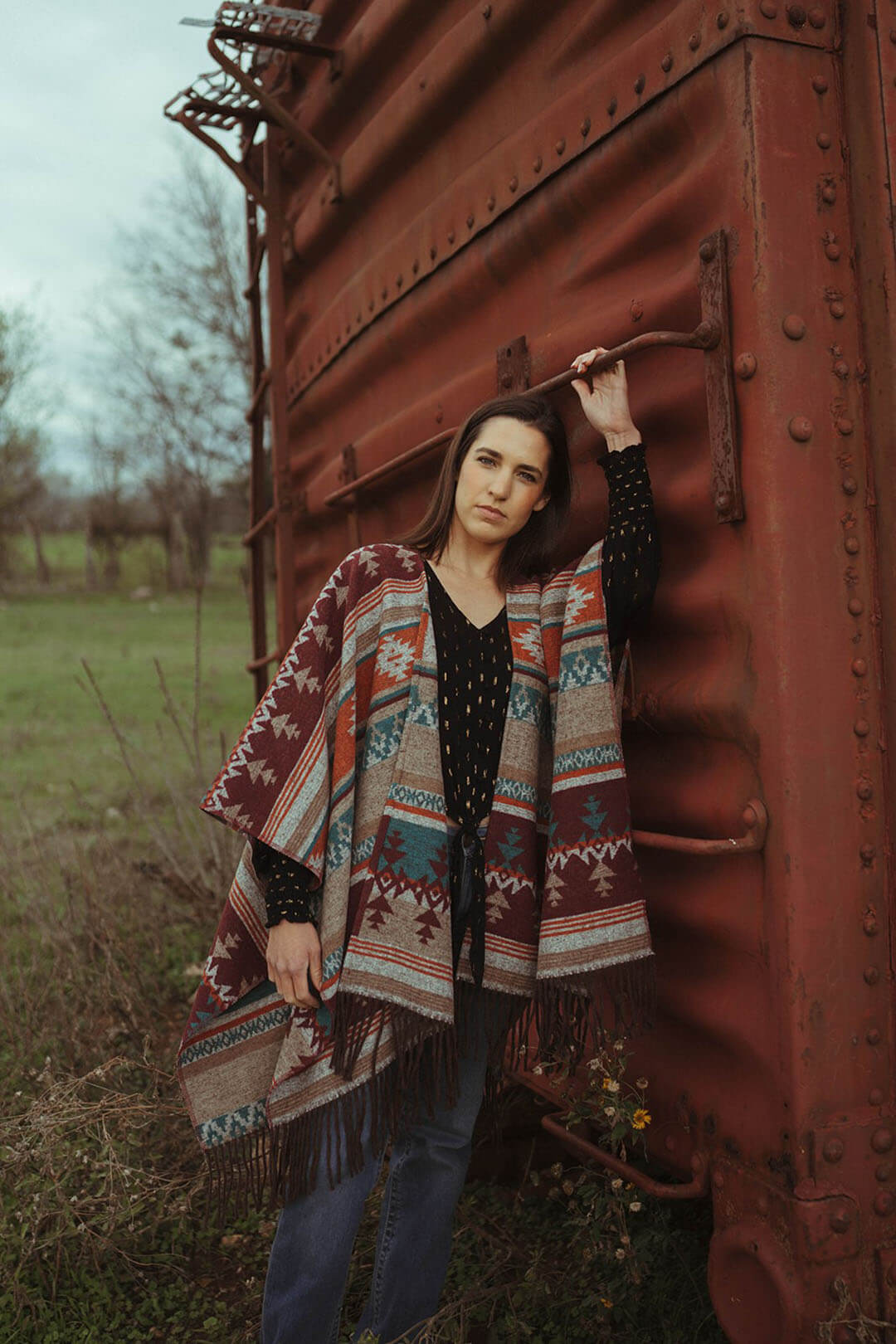 Woman modeling the cripple creek aztec poncho.  The poncho features orange, cream ,and blue colors throughout .  Beautiful detail
