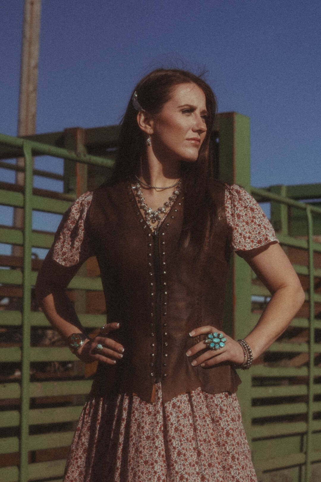 Woman standing in arena modeling the Cripple Creek Womens Antique Finish Stud Vest.  Vest features stud details by the zip closure on each side. 