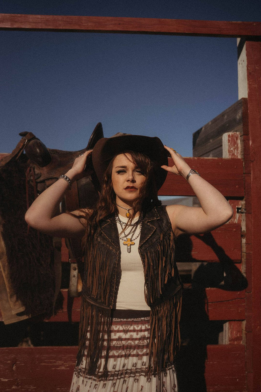 Woman standing in corral modeling the Cripple Creek Womens Fringe Leather Vest.  The vets is brown in color.