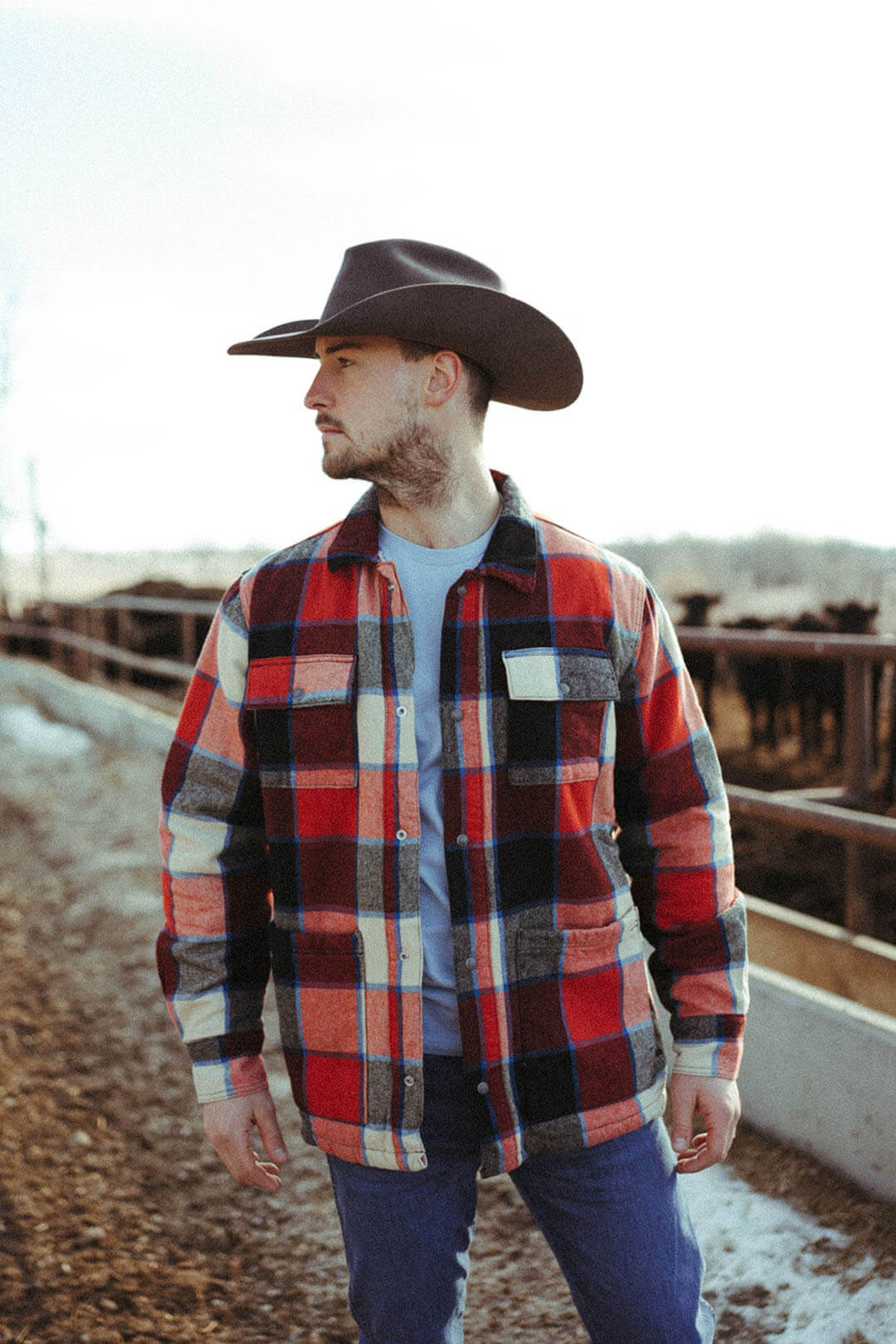 Man standing in corral wearing the Wrangler Flannel Sherpa Jacket.  The jacket is collared and is snap button up closure.
