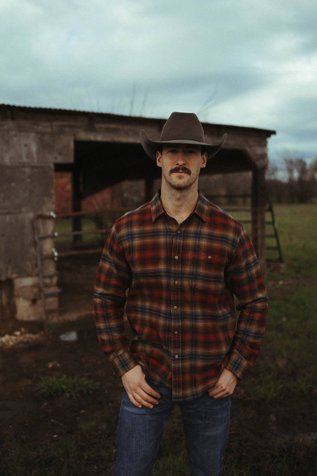 Man modeling the copper/navy color of the fremont flannel pendleton button up shirt.  The shirt is long sleeve . 