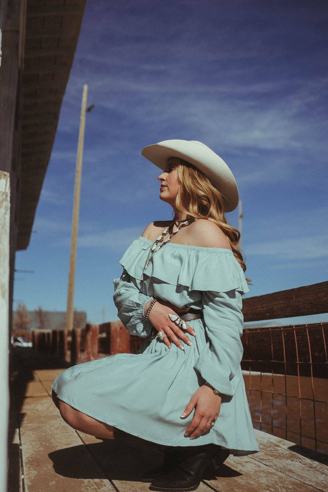 Woman kneeling down showing the Off the Shoulder Mint Wrangler Dress.  Long sleeve dress with elastic cuffs. 