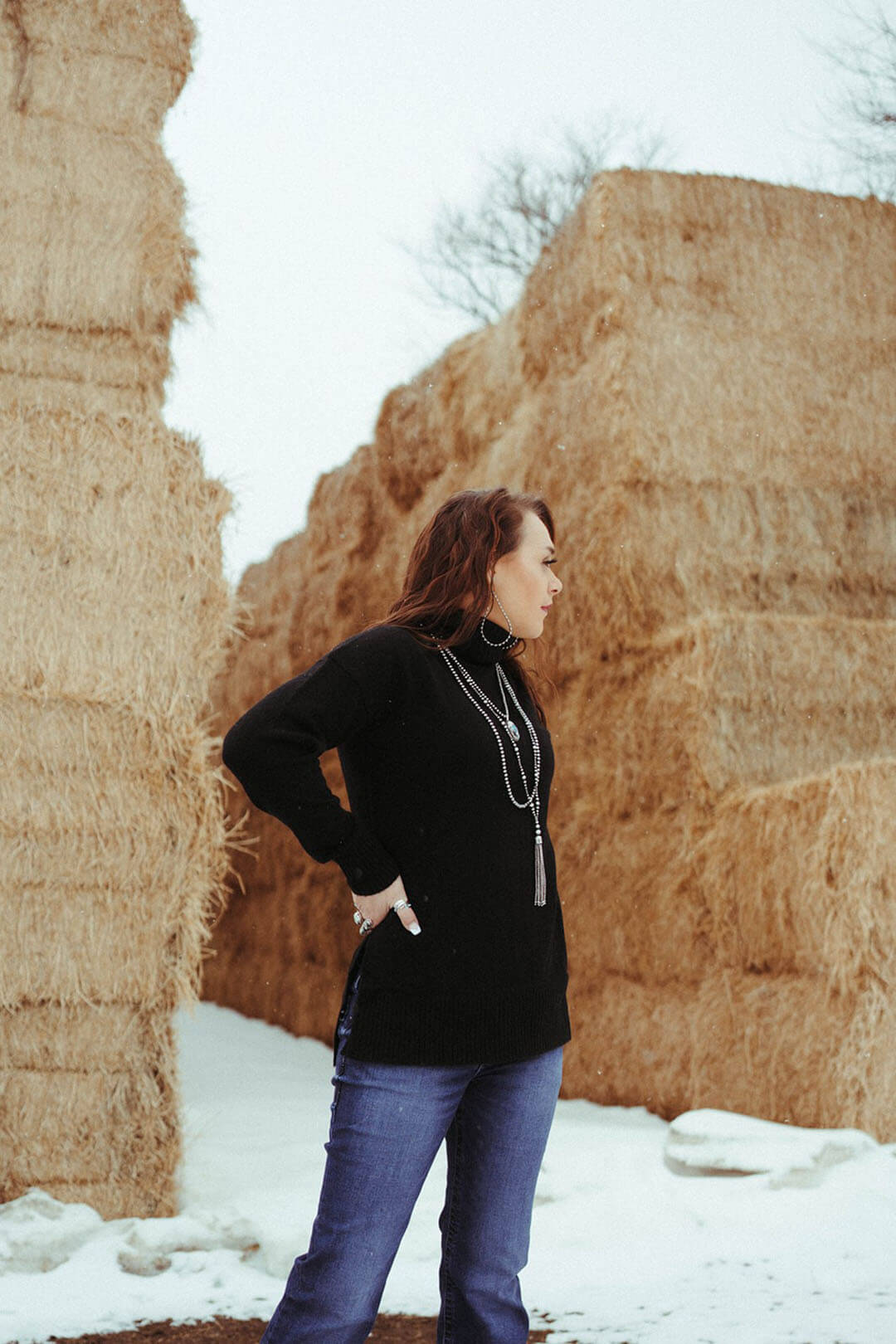 Woman standing near hay bales modeling the Pendleton Womens Oversized Turtleneck.  She is pictured wearing the black colored one. 