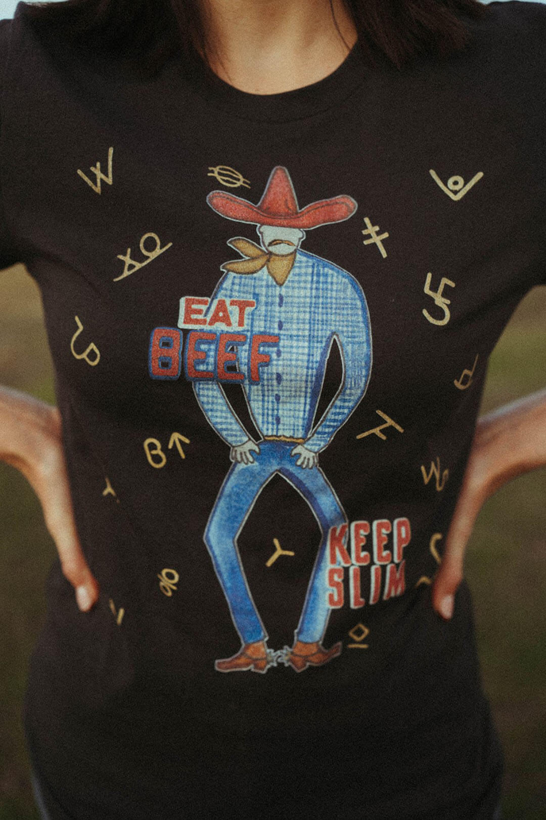 Close up picture of the XOXO art & company graphic tee featuring cow branding logos throughout and a cowboy with the saying "Eat Beef, Keep Slim"