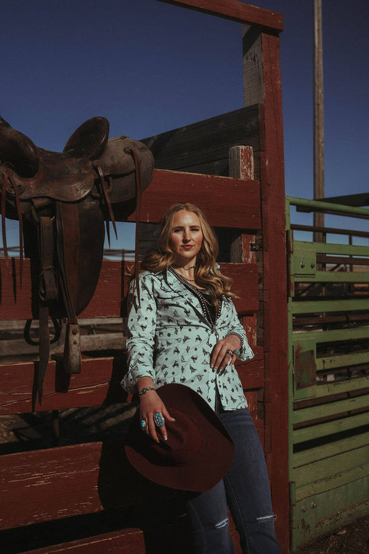 Woman standing in corral wearing the Wild West Wrangler Pearl Snap Shirt.  The shirt is long sleeve and is a light blue color.