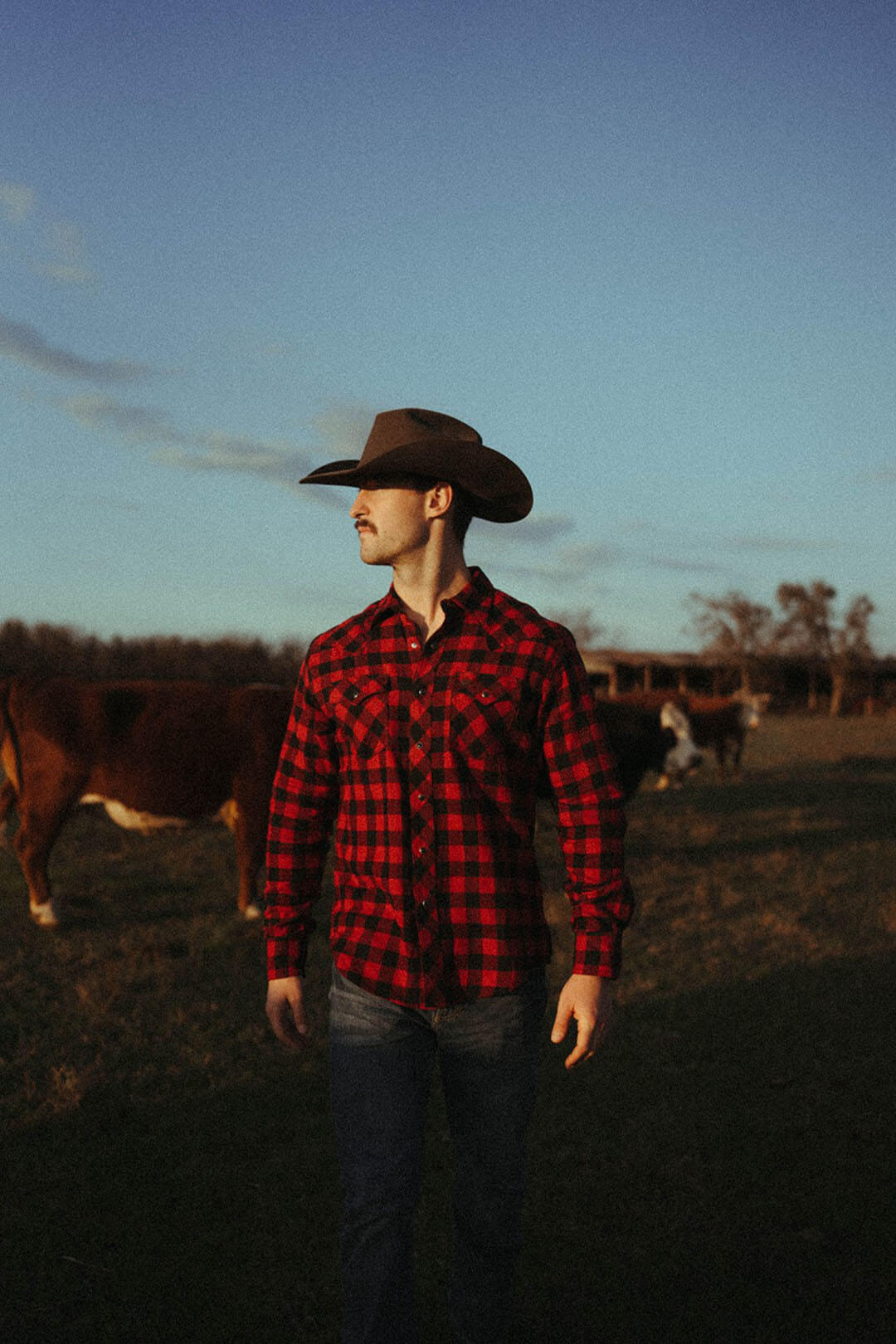 Man standing in field modeling the wrangler mens retro buffalo long sleeve pearl snap shirt. 