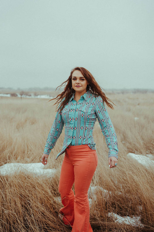 Woman standing in field wearing the Wrangler Retro Green Aztec Top.  The top is pearl snap.