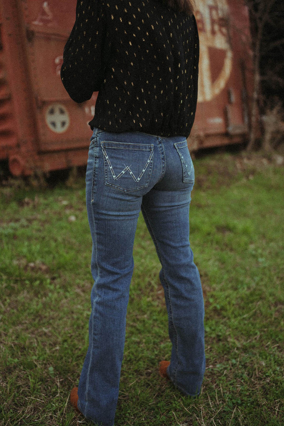 Woman modeling the back of the wrangler willlow nelllie wash bootcut jean.  The jeans have 2 back pockets and have the "W' emblem on each pocket.