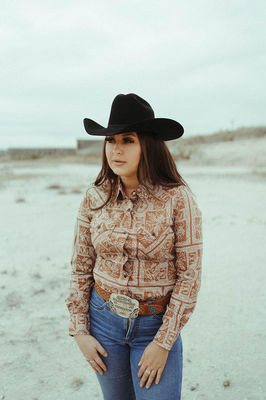 Woman modeling the womens western scene pearl snap shirt by wrangler.  The shirt is a lighter brown color with white outlines of  western scene.  
