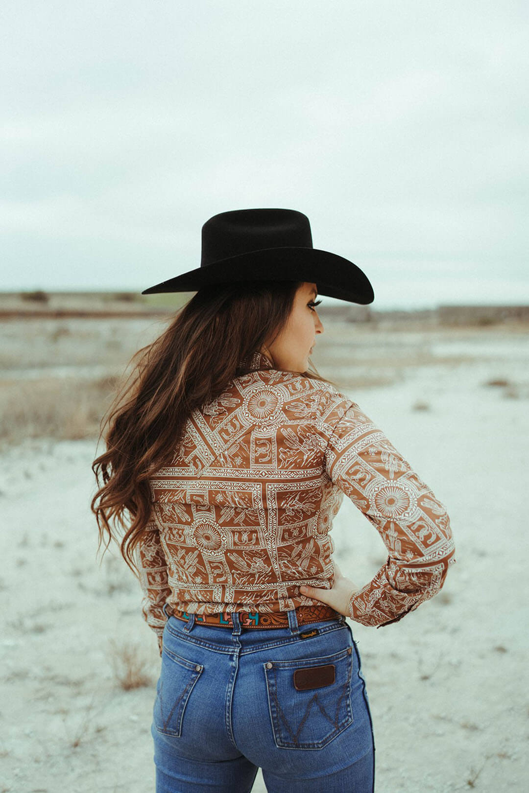 Woman wearing the wrangler western scene pearl snap shirt.  This shirt is unique with different western emblems throughout. 