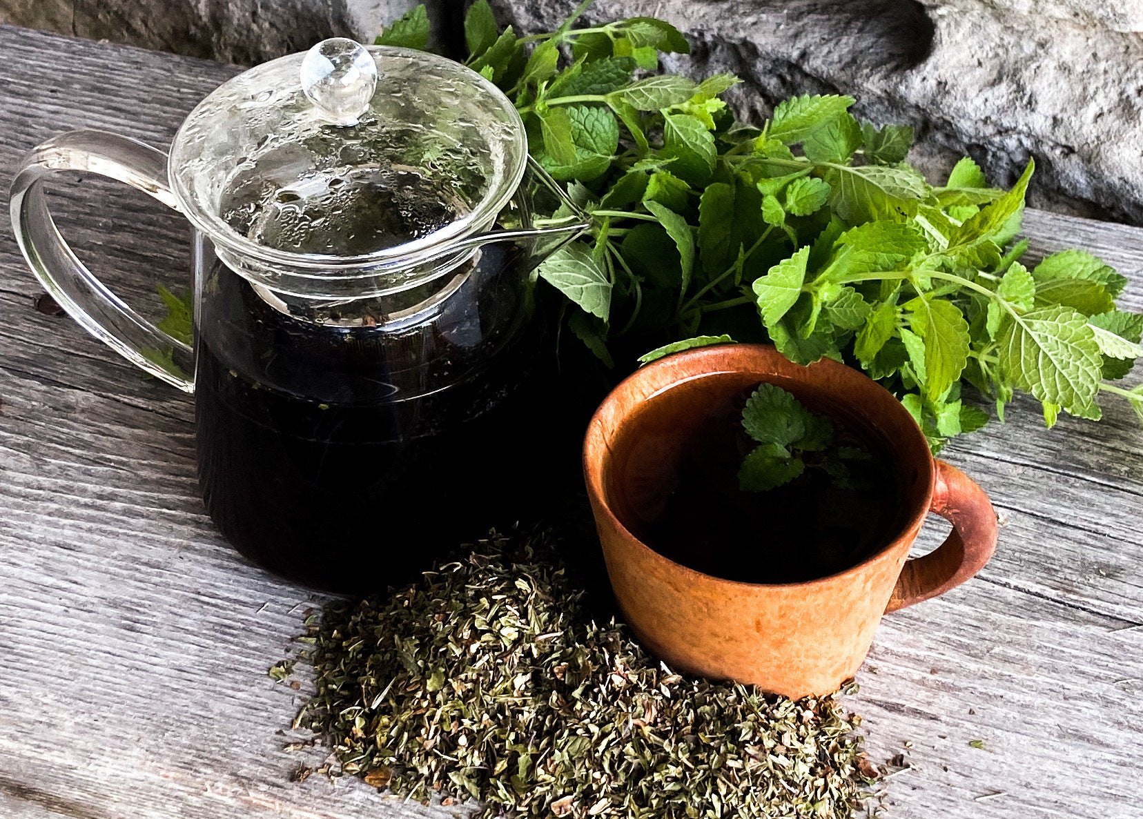 Clear glass teapot and red mug with peppermint tea and loose peppermint leaves