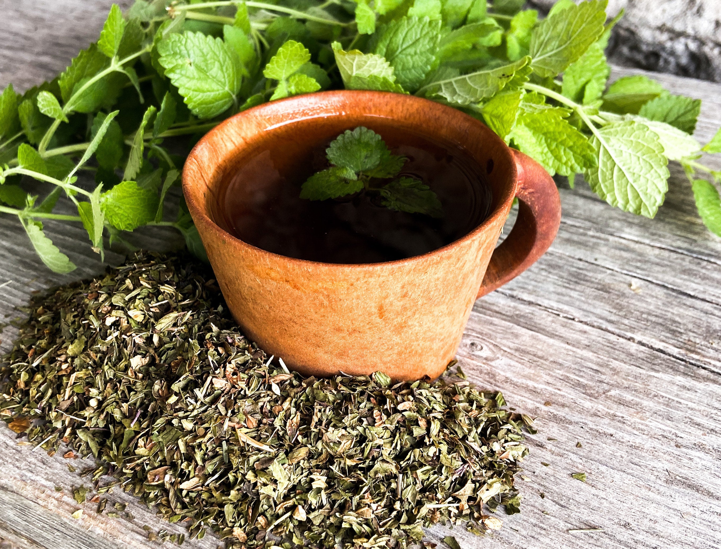 A red teacup with loose peppermint leaves and fresh peppermint