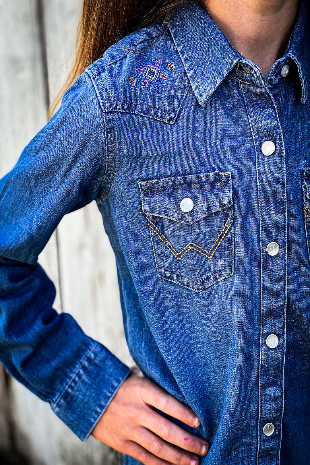 Close up picture of the girls wrangler denim pearl snap shirt.  The shirt features aztec symbol on shoulder. 