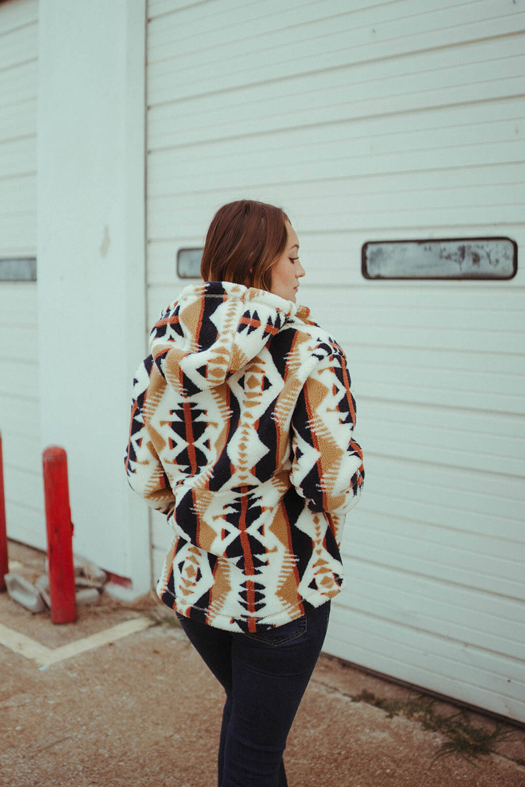 Woman modeling the back of the pendleton fleece hooded jacket.  The jacket has different colors of cream, blue, and orange and has aztec design throughout. 