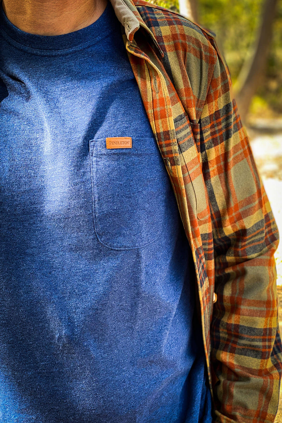 Man wearing Pendleton Deschutes Pocket Tee in a heather navy blue with outer layered button up Pendleton long sleeve yellow orange and blue shirt