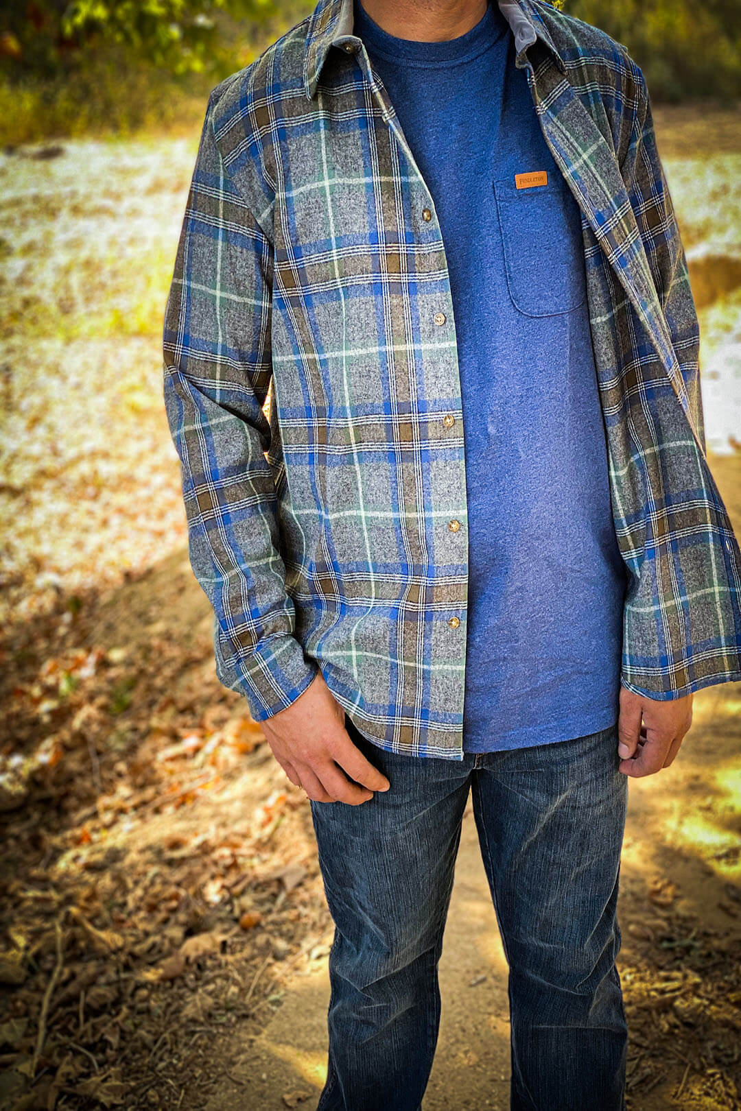 Man wearing Pendleton lodge long sleeve blue, gray striped plaid pattern with button front with blue Pendleton shirt underneath and denim jeans