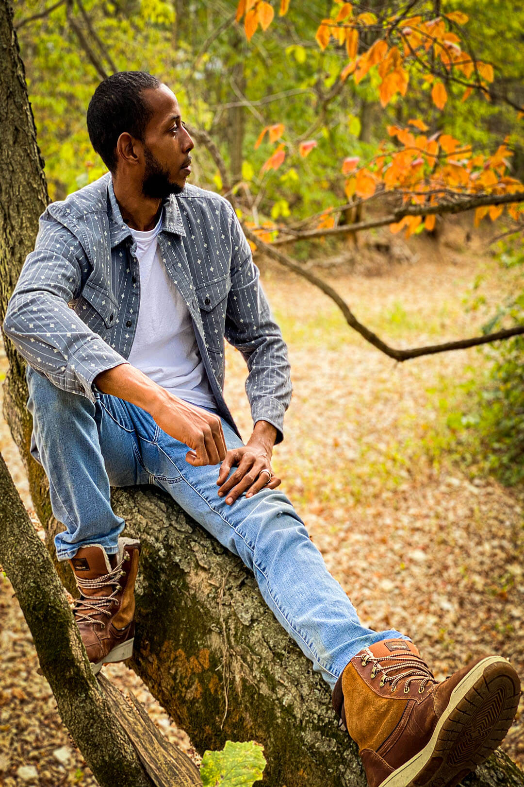 Man wearing corduroy long sleeved shirt gray with small white diamond and line pattern button up front with front pockets sitting in tree denim jeans