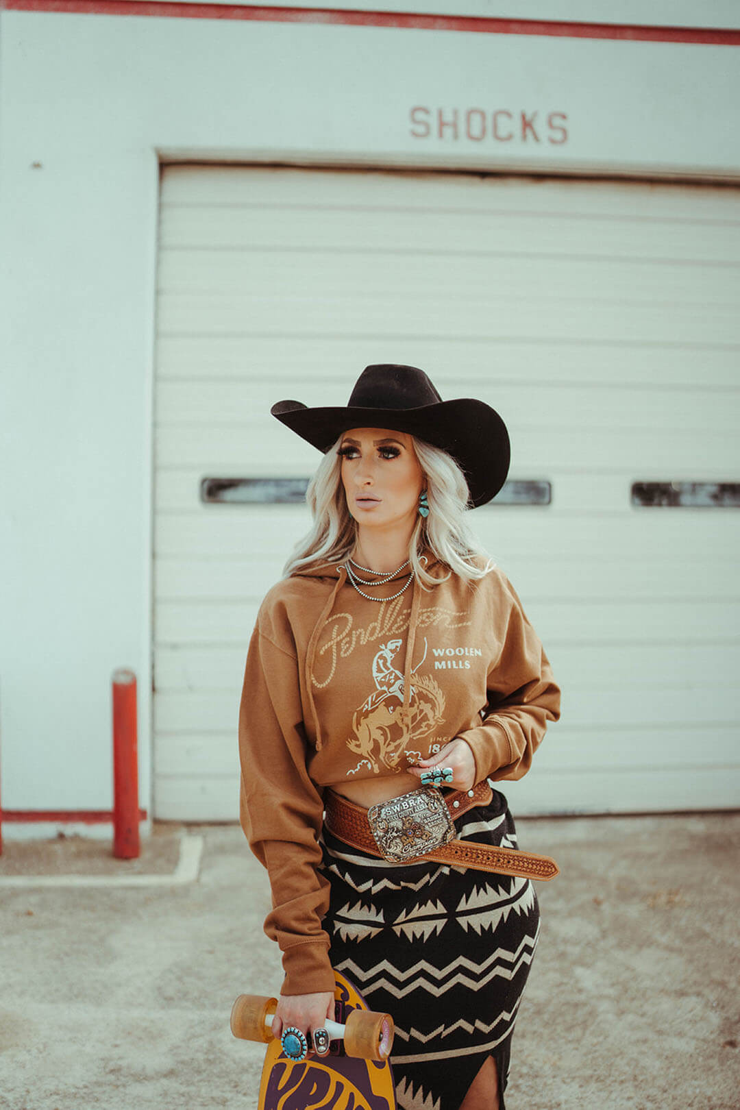 Woman wearing the Pendelton Woolen Mills Rodeo hoodie in Gold color.  The hoodie features a scene of cowboy riding a bronc.  