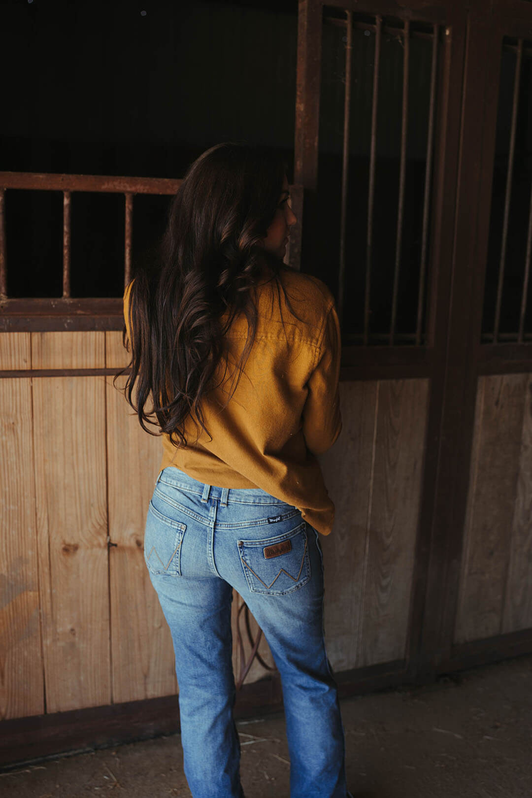 Woman modeling the back of the wrangler retro mid rise bootcut jeans.  The jeans feature the "W" stitching on each side. 