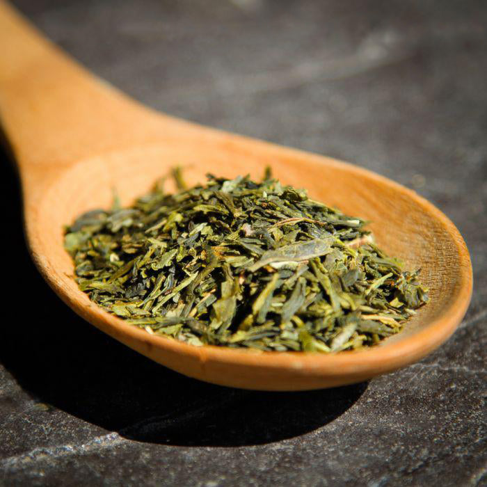 A closeup of Sencha Green Tea on a wooden spoon, on a dark surface.
