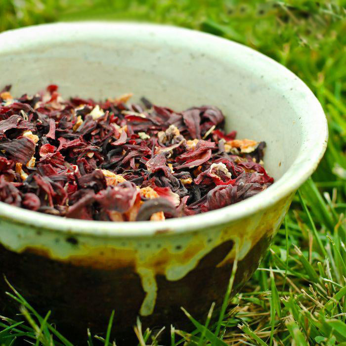 Hibiscus Orange Tea is in a brown and white bowl that has been placed on the grass.